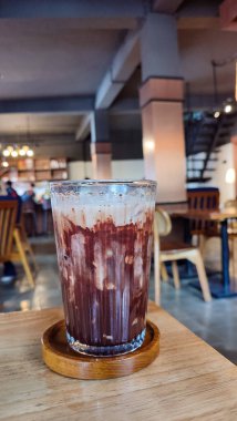 Buzlu çikolatayı yakın çekimde, modern kafede, ahşap masada servis edilir. Buzlu iç döşeme ahşap mobilyalar ve yumuşak ışıklandırma içeriyor..