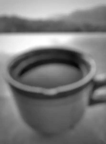 Bokeh. Seramik bir masada bir bardak sade kahvenin yakın çekimi. Bokeh doğa geçmişi var. Siyah ve beyaz