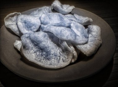 Siyah ve beyaz. Manzara, arka planda fayans zemini olan turuncu renkli bir tabakta beyaz kraker yığını. Kerupuk putih, ya da bilinen adıyla, Kerupuk prasmanan.