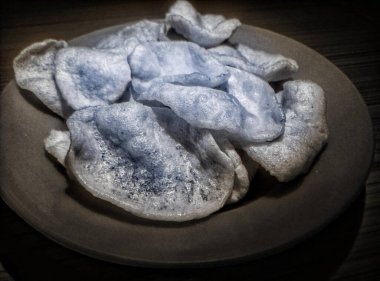 Siyah ve beyaz. Manzara, arka planda fayans zemini olan turuncu renkli bir tabakta beyaz kraker yığını. Kerupuk putih, ya da bilinen adıyla, Kerupuk prasmanan.