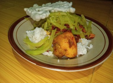 Horizontal, Indonesian home cooking. A plate of white rice, chayote vegetables, white crackers and chicken sambal sits on a tiled floor in the background. clipart