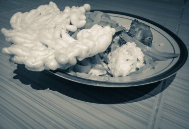 Black and white, retro. A plate of white rice, chayote vegetables, white crackers and chicken sambal sits on a plate in front of a plate of rice on the floor. The room has tiles on the floor. clipart