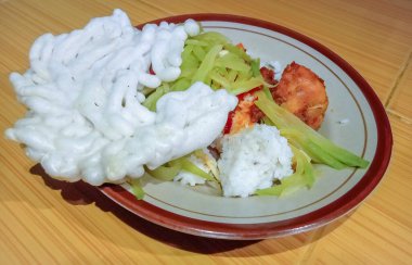 Yerdeki bir tabak pirincin önünde bir tabak beyaz pirinç, chayote sebzesi, beyaz kraker ve tavuk sambal var. Zemin kiremitli..