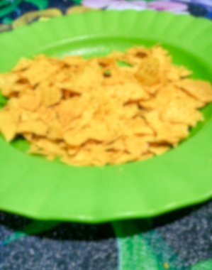 Yeşil plastik tabakta sarı cips, bulanık..