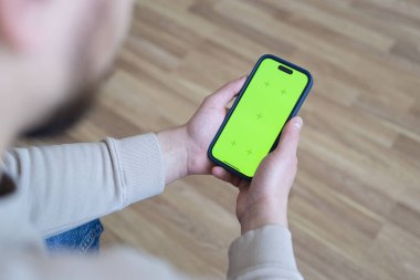 Evdeki adam kanepede uzanmış yeşil ekran ekranlı akıllı telefon kullanıyor, kaydırmalı hareketler yapıyor. Cep telefonu, internet sosyal ağları kullanan bir adam. Sosyal medya.