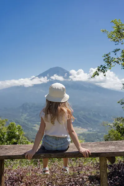 小さな女の子の子供がベンチに座って火山を見て 旅行の概念 — ストック写真