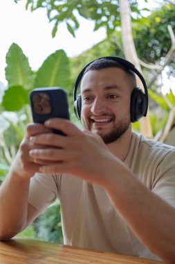 Gündelik giysiler içinde, iş yerinde çalışan, kulaklık takan genç, mutlu, yaratıcı, serbest bir adam. Bali tropikal adasında uzaktan çalışma, taşınma