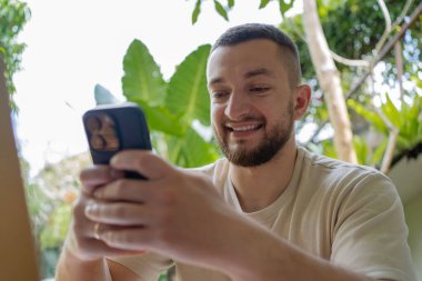 Güzel bir terasta dizüstü bilgisayarla çalışan bir adam. Dizüstü bilgisayarı olan adam Bali 'de yaz tatilinde eğleniyor. İnternette açık havada gülümseyen dijital erkek göçebe. Serbest çalışan. .