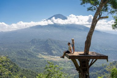 Baba ve kız turistler Endonezya 'daki Bali adasını geziyorlar. Agung Dağı manzaralı ağacın üzerinde dururlar.