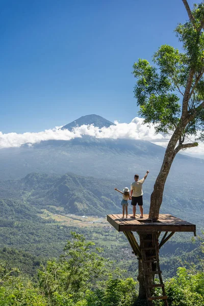 インドネシアのバリ島を旅行する父と娘の観光客 彼らはアグン山を眺めながら木の上の写真の場所に立っています — ストック写真