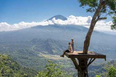 Baba ve kız turistler Endonezya 'daki Bali adasını geziyorlar. Agung Dağı manzaralı ağacın üzerinde dururlar.