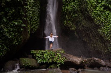 Ormanda şelalenin önünde duran bir kadın. Endonezya 'yı gezmek. Adanın gizli güzelliği