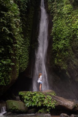 Ormanda şelalenin önünde duran bir kadın. Endonezya 'yı gezmek. Adanın gizli güzelliği
