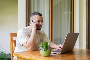 Freelancer çalışanı telefonla konuşuyor, dizüstü bilgisayar kullanıyor, ekrana bakıyor, girişimci yöneticiye telefonla danışıyor, bilgisayar ekranına bakıyor, projeyi tartışıyor, bilgi okuyor..