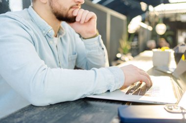 Genç yakışıklı adam kafede oturuyor, dizüstü bilgisayar kullanıyor ve daktilo ediyor. Kafede bilgisayar kullanan yakışıklı hippi.