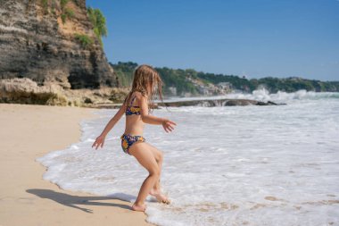 Gülümseyen kız çocuk bir aile tatilinde sahilde koşuyor ve oynuyor. Okyanus dalgalarında oynamak eğlenmek ve aktif olmak..