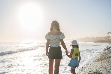 Anne ve kızı güneşli bir günde dalgalara bakın.