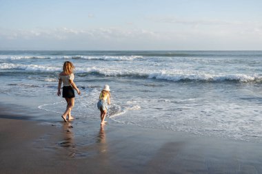 Anne ve kızı Bali 'de kumsalda eğleniyorlar, dalgalarda koşuyorlar, hayatın tadını çıkarıyorlar ve seyahat ediyorlar.