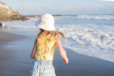  Bali 'deki tropik deniz sahillerinde iyi eğlenceler. Sörf kenarındaki su birikintisinin yanında koşan komik kız. Aktif çocuk yaşam tarzı. 