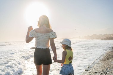 Anne ve kızı güneşli bir günde dalgalara bakın.