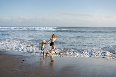 Anne ve kızı Bali 'de kumsalda eğleniyorlar, dalgalarda koşuyorlar, hayatın tadını çıkarıyorlar ve seyahat ediyorlar.