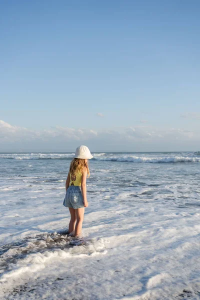  Bali 'deki tropik deniz sahillerinde iyi eğlenceler. Sörf kenarındaki su birikintisinin yanında koşan komik kız. Aktif çocuk yaşam tarzı. 