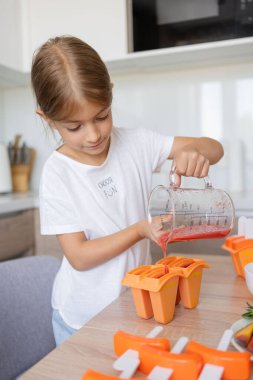 Dondurma yapma süreci. Mutfaktaki tezgahın üstündeki kalıplarda leziz buz lolipopları yapan bir çocuk..