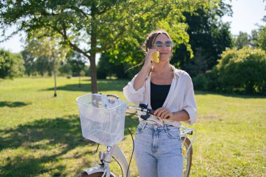 European young woman in park with bicycle and talking on mobile phone. 
