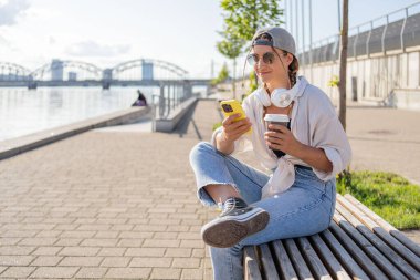 Genç İspanyol hippi kız elinde içecekle sokakta otururken cep telefonunu karıştırıyor.. 