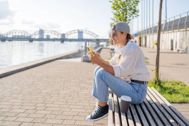 Genç İspanyol hippi kız elinde içecekle sokakta otururken cep telefonunu karıştırıyor.. 