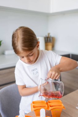 Dondurma yapma süreci. Mutfaktaki tezgahın üstündeki kalıplarda leziz buz lolipopları yapan bir çocuk..