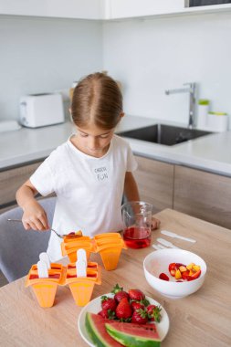 Dondurma yapma süreci. Mutfaktaki tezgahın üstündeki kalıplarda leziz buz lolipopları yapan bir çocuk..