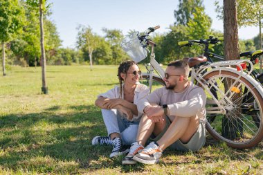 Bisiklet sürdükten sonra genç ve mutlu bir çift parkta birlikte vakit geçiriyor.