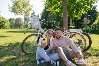 Bisiklet sürdükten sonra genç ve mutlu bir çift parkta birlikte vakit geçiriyor.
