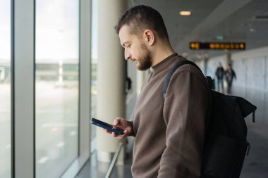 Turist bekleme salonunda yerini almakla meşgul. Havaalanında uçak beklerken cep telefonlu genç bir adam.