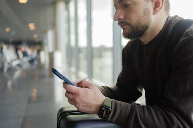 Turist bekleme salonunda yerini almakla meşgul. Havaalanında uçak beklerken cep telefonlu genç bir adam.