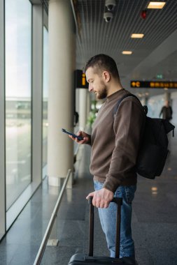 Turist bekleme salonunda yerini almakla meşgul. Havaalanında uçak beklerken cep telefonlu genç bir adam.