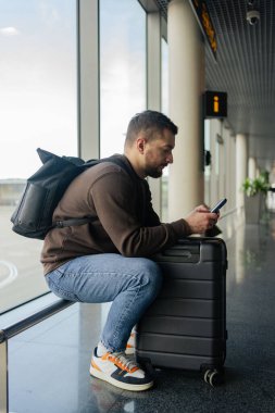 Turist bekleme salonunda yerini almakla meşgul. Havaalanında uçak beklerken cep telefonlu genç bir adam.