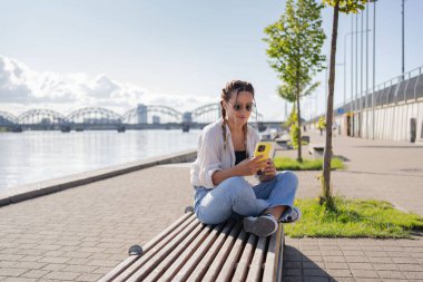 Şehir caddesinde oturan hippi bir kadın, selofan kullanıyor, arkadaşlarıyla sohbet ediyor, video görüşmesi yapıyor.