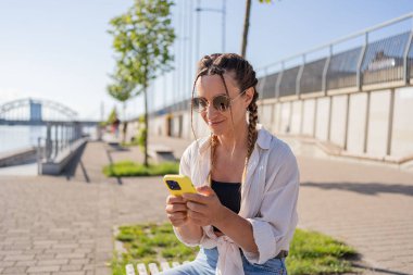 Şehir caddesinde oturan hippi bir kadın, selofan kullanıyor, arkadaşlarıyla sohbet ediyor, video görüşmesi yapıyor.