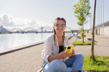 Şehir caddesinde oturan hippi bir kadın, selofan kullanıyor, arkadaşlarıyla sohbet ediyor, video görüşmesi yapıyor.