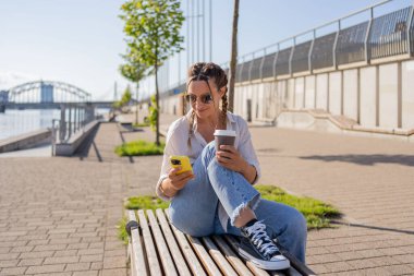 Şehir caddesinde oturan hippi bir kadın, selofan kullanıyor, arkadaşlarıyla sohbet ediyor, video görüşmesi yapıyor.