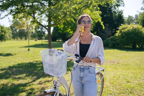 European young woman in park with bicycle and talking on mobile phone.