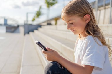 Şehirde sokakta oturan kız çocuğu cep telefonu kullanıyor.. 