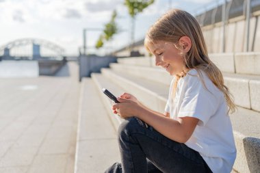 Şehirde sokakta oturan kız çocuğu cep telefonu kullanıyor.. 