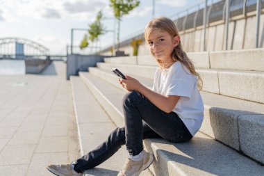 Şehirde sokakta oturan kız çocuğu cep telefonu kullanıyor.. 