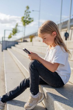 Şehirde sokakta oturan kız çocuğu cep telefonu kullanıyor.. 