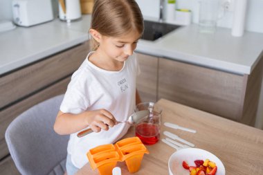 Dondurma yapma süreci. Mutfaktaki tezgahın üstündeki kalıplarda leziz buz lolipopları yapan bir çocuk..