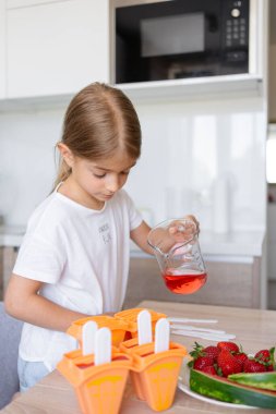 Dondurma yapma süreci. Mutfaktaki tezgahın üstündeki kalıplarda leziz buz lolipopları yapan bir çocuk..