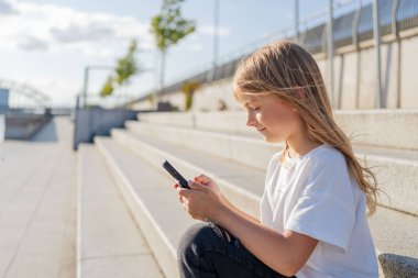 Şehirde sokakta oturan kız çocuğu cep telefonu kullanıyor.. 